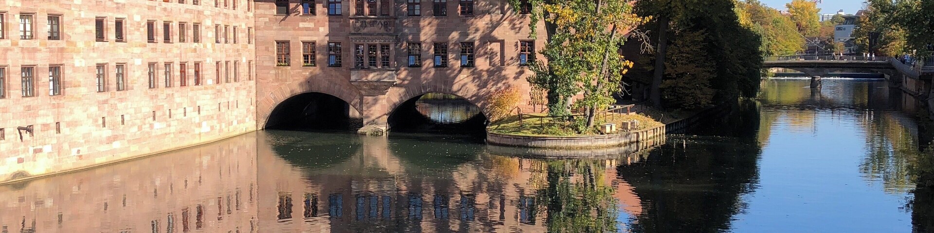 A historic building with a bridge over a calm river, surrounded by autumn foliage.