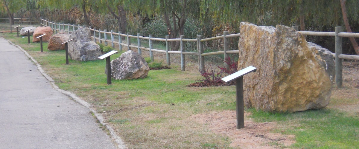 A pathway lined with large rocks and a wooden fence, with trees in the background.