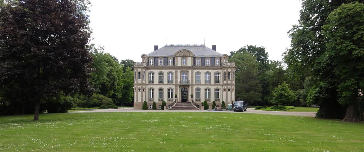A large, historic building with a symmetrical facade, surrounded by a well-maintained lawn and trees.