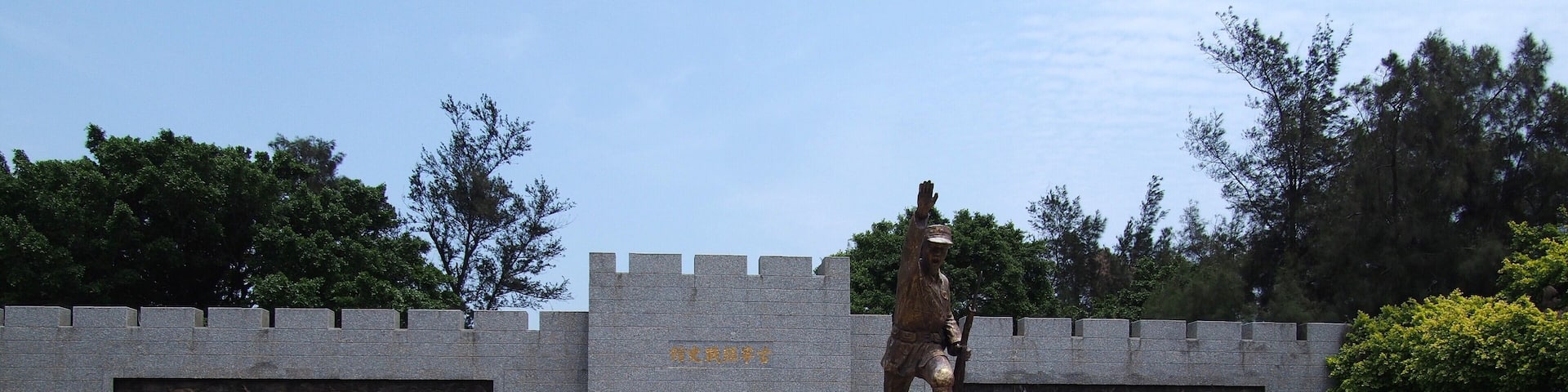 A statue in a courtyard with a stone wall featuring reliefs and a plaque.