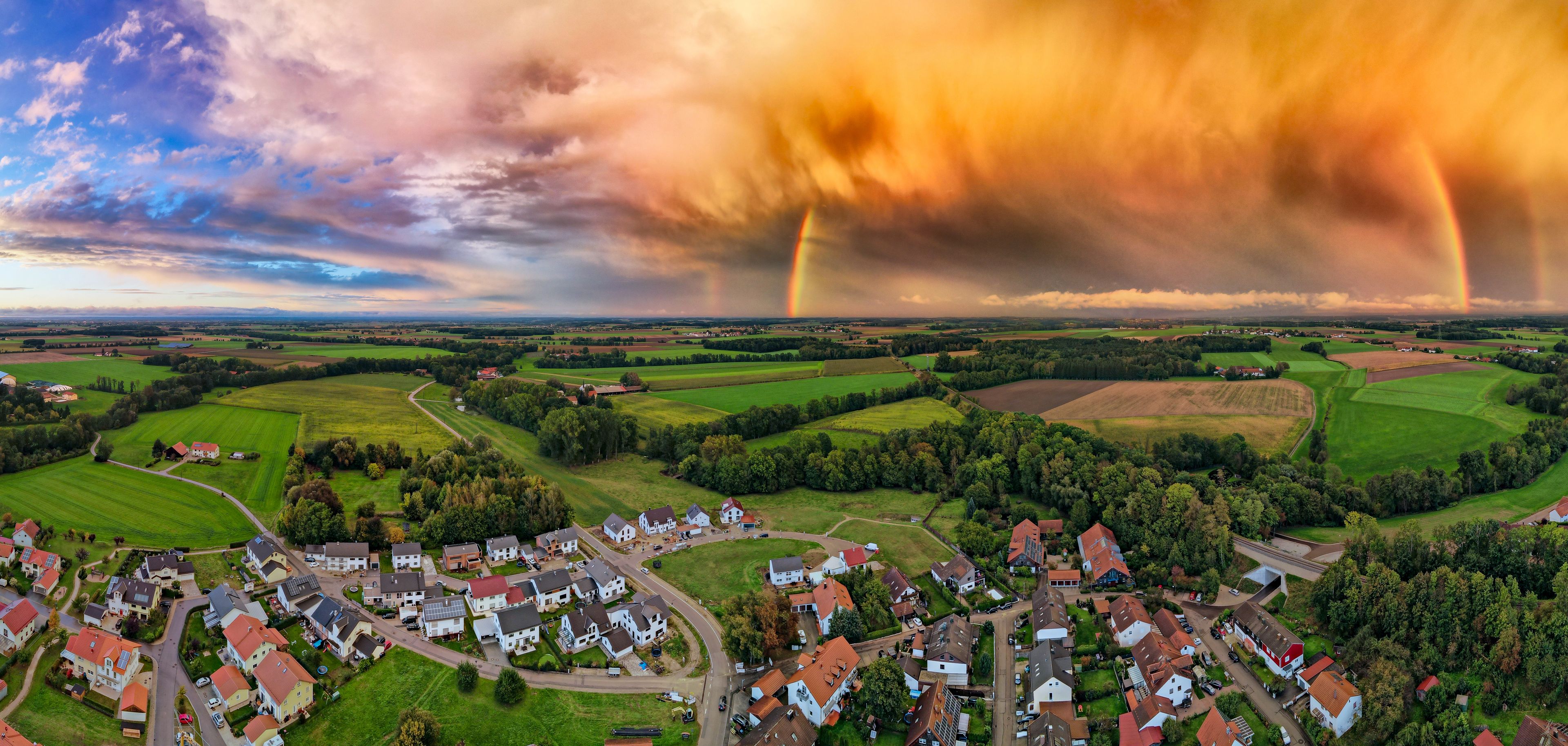 Un paysage rural avec des champs, un petit village et un arc-en-ciel.