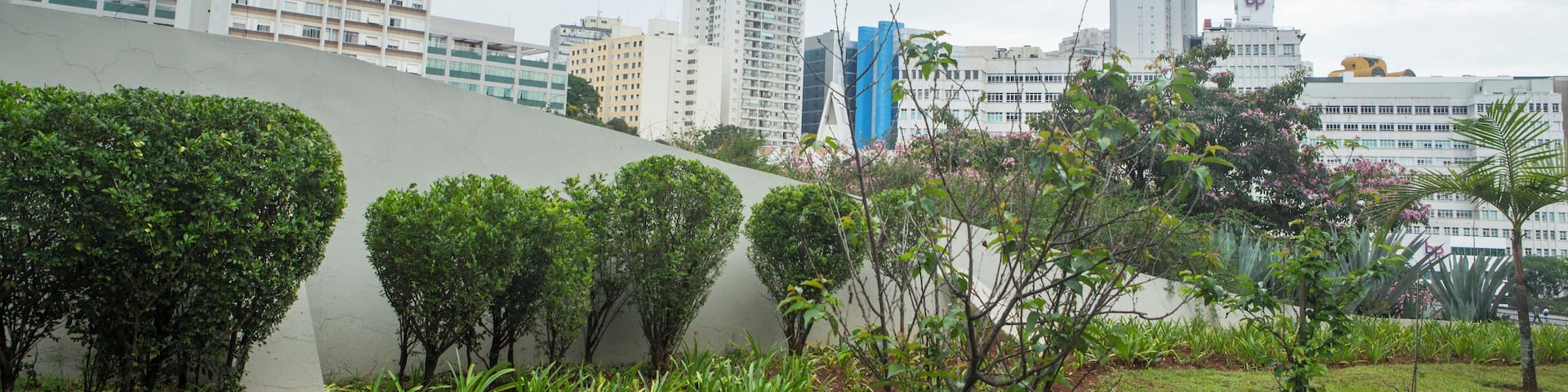 A cityscape with modern buildings, a curved wall, and a grassy area with small trees.