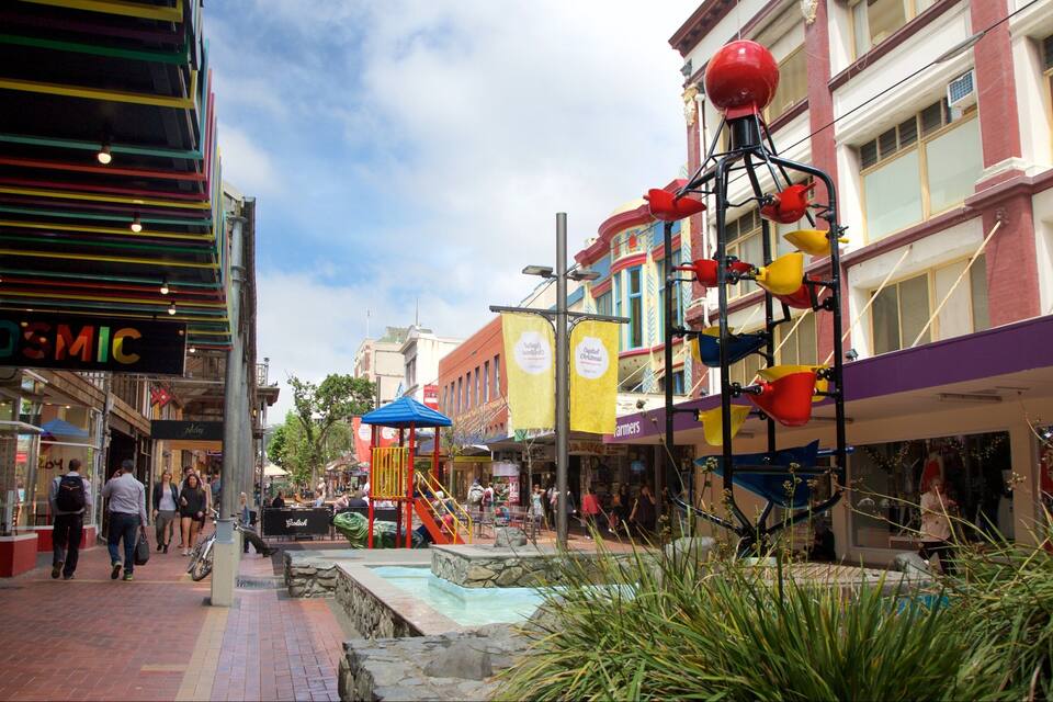 Une rue animée, bordée d’immeubles aux couleurs vives, avec une aire de jeux et une petite fontaine.