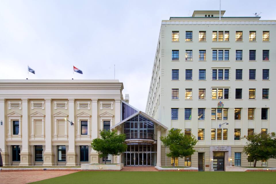 A large, historic building with classical architecture, a modern glass structure, and a flagpole with multiple flags.