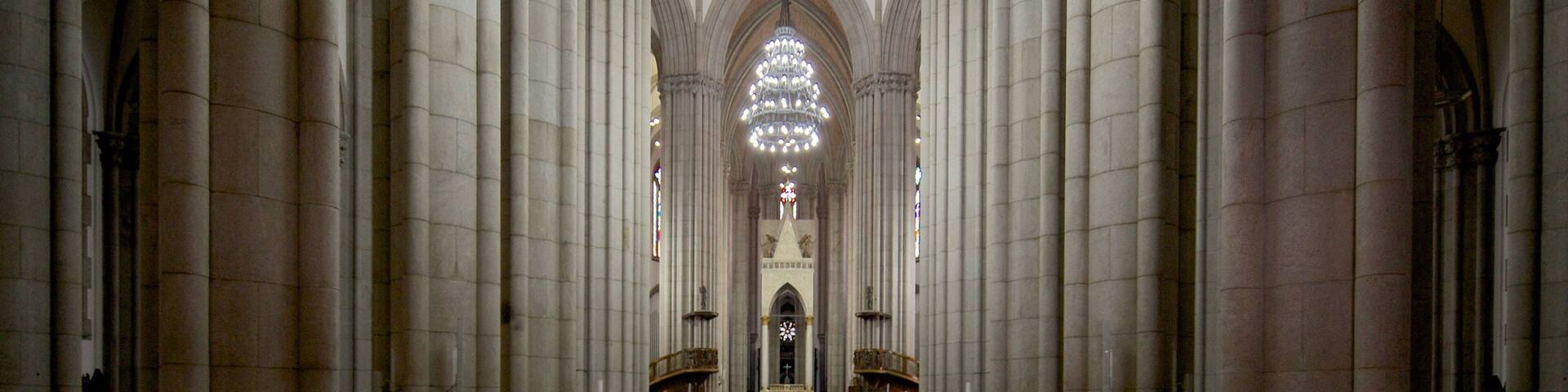 A cathedral interior with tall columns, a large chandelier, and stained glass windows.
