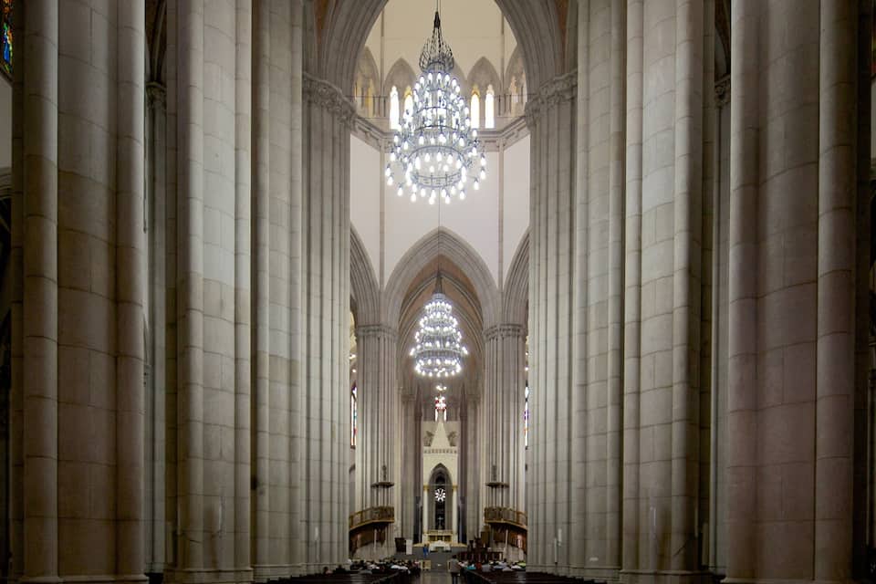 Ein Kathedralinnenraum mit hohen Säulen, einem großen Chandelier und Buntglasfenstern.