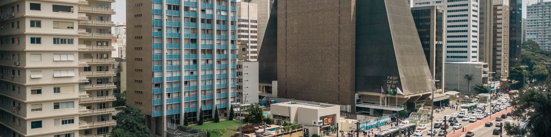 Paisagem urbana com edifícios altos, um cruzamento movimentado e um ônibus verde.