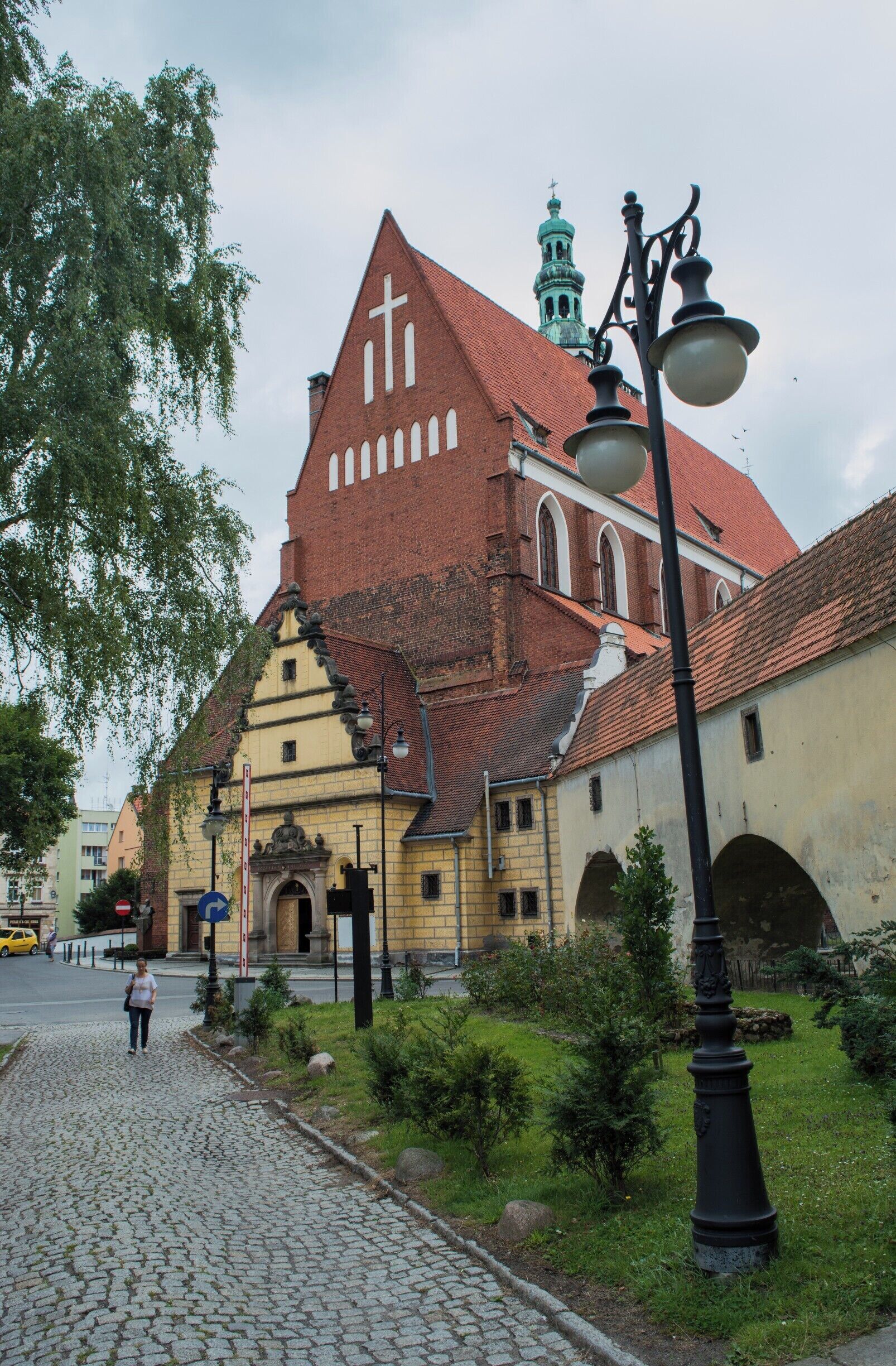 A historic church with a red roof and a cross on the facade, a cobblestone street, and a lamppost.