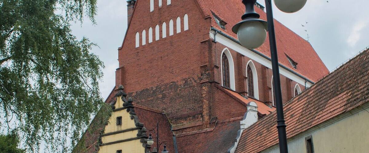 A historic church with a red roof and a cross on the facade, a cobblestone street, and a lamppost.