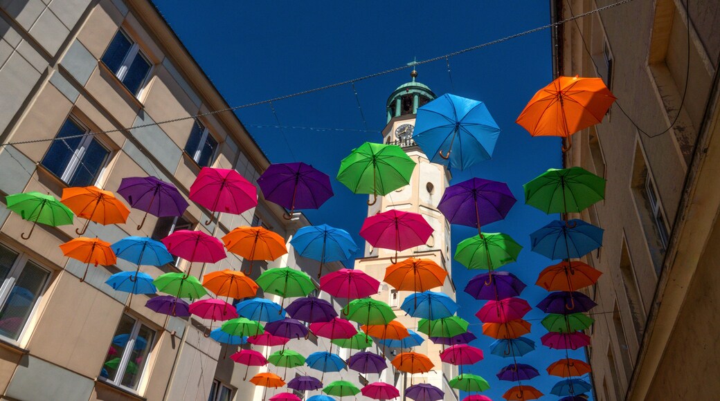 Multi-colored umbrellas hanging between buildings leading towards an old white city clock tower. Olesnica, Poland