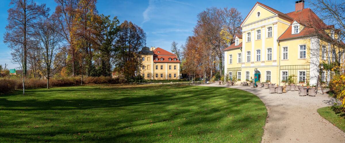 A well-maintained lawn, a yellow building with a red roof, and a large tree in the background.
