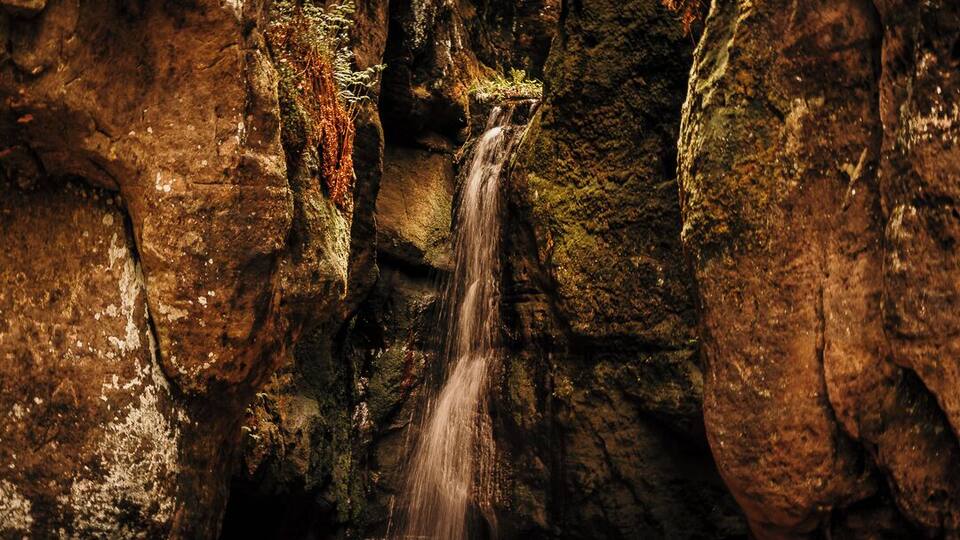 A waterfall in a rocky cave with moss-covered walls.