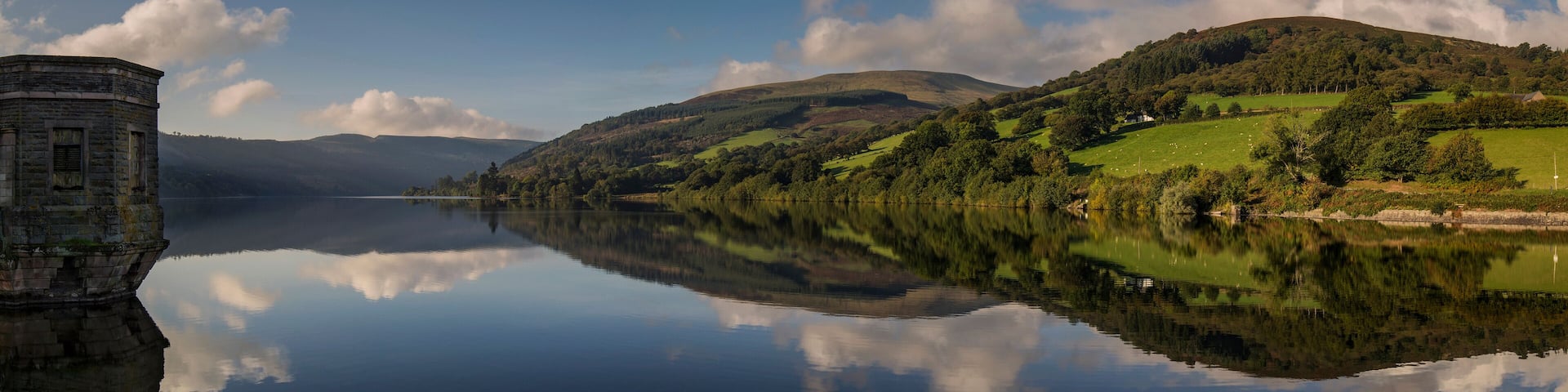 A calm lake with a stone tower on the left, surrounded by green hills and a clear sky.