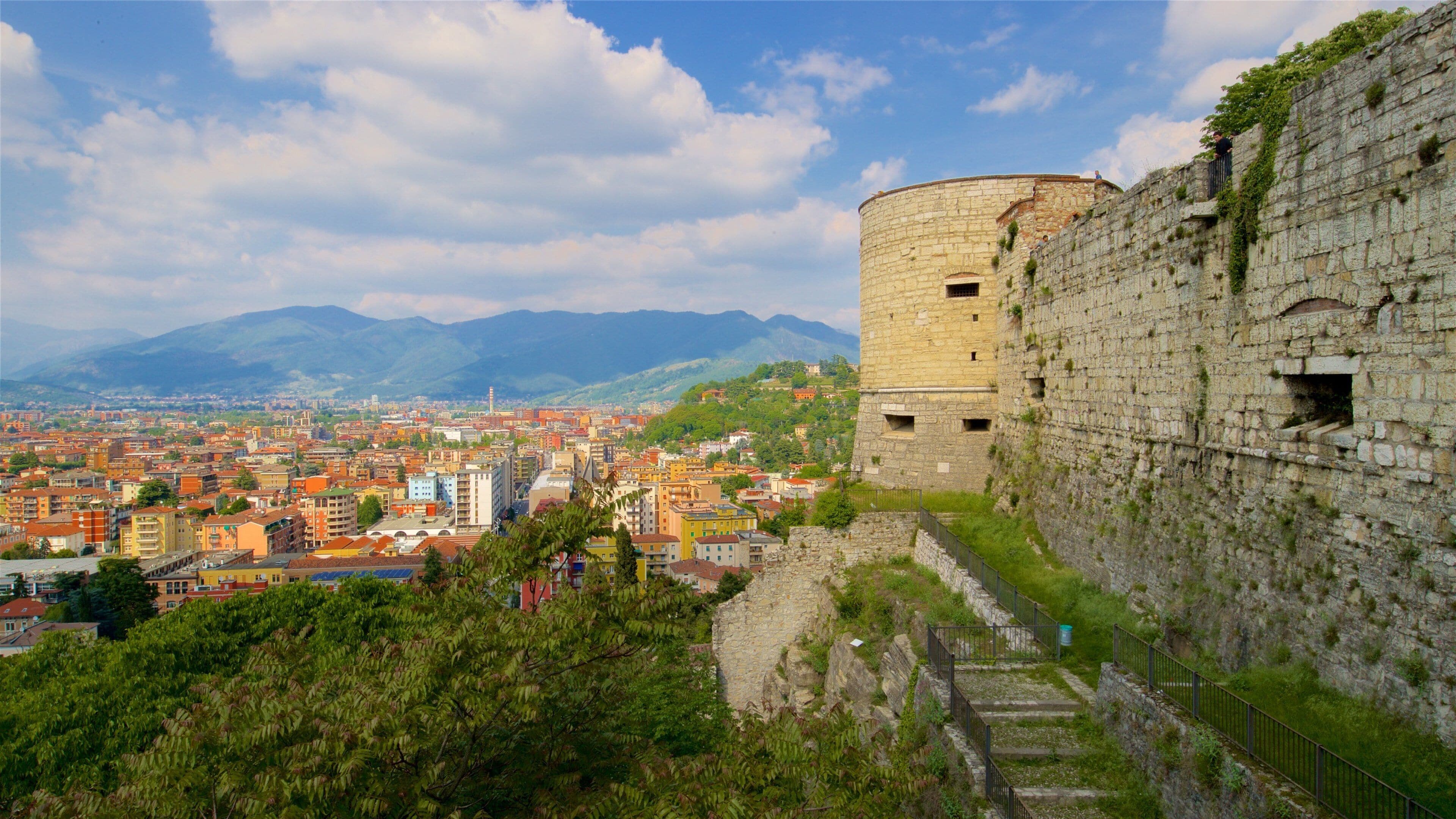 A historic stone tower overlooking a city with colorful buildings and mountains in the background.