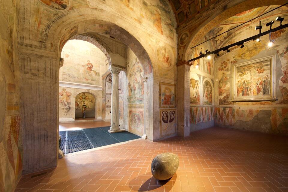 An interior with arched ceilings, frescoes, and a stone sculpture on the floor.