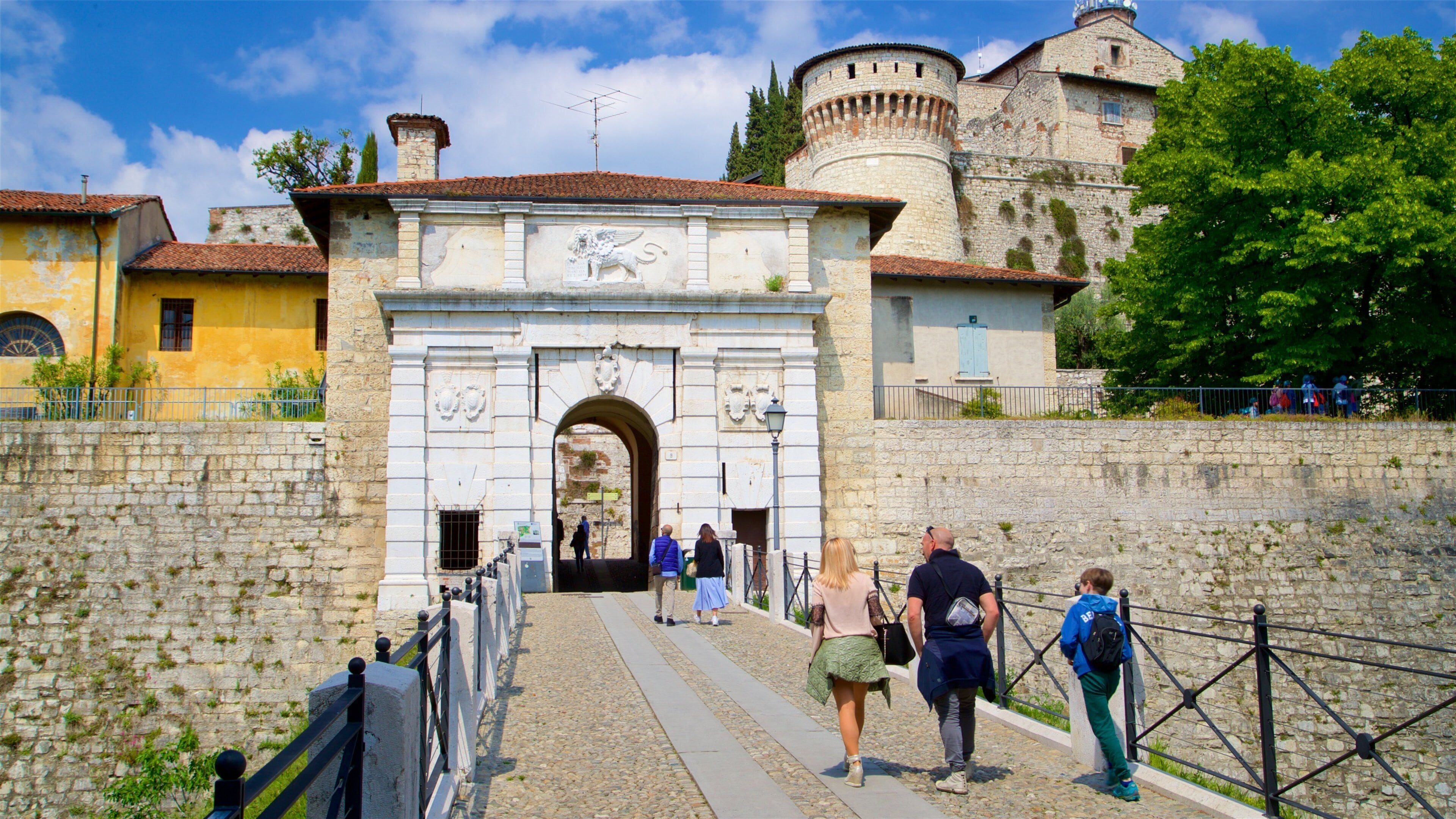 A historic stone archway leading to a castle, with tourists walking through.