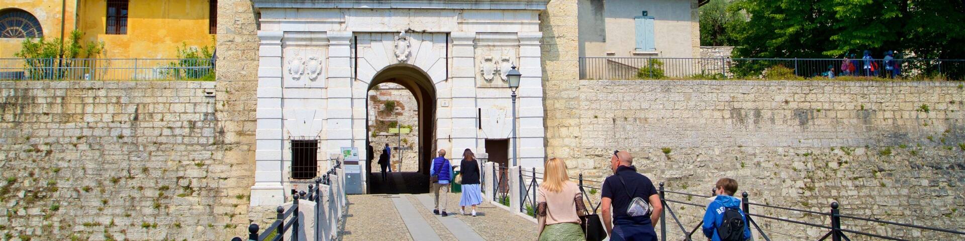 Un arc en pierre d’époque, menant à un château, où des touristes se promènent.