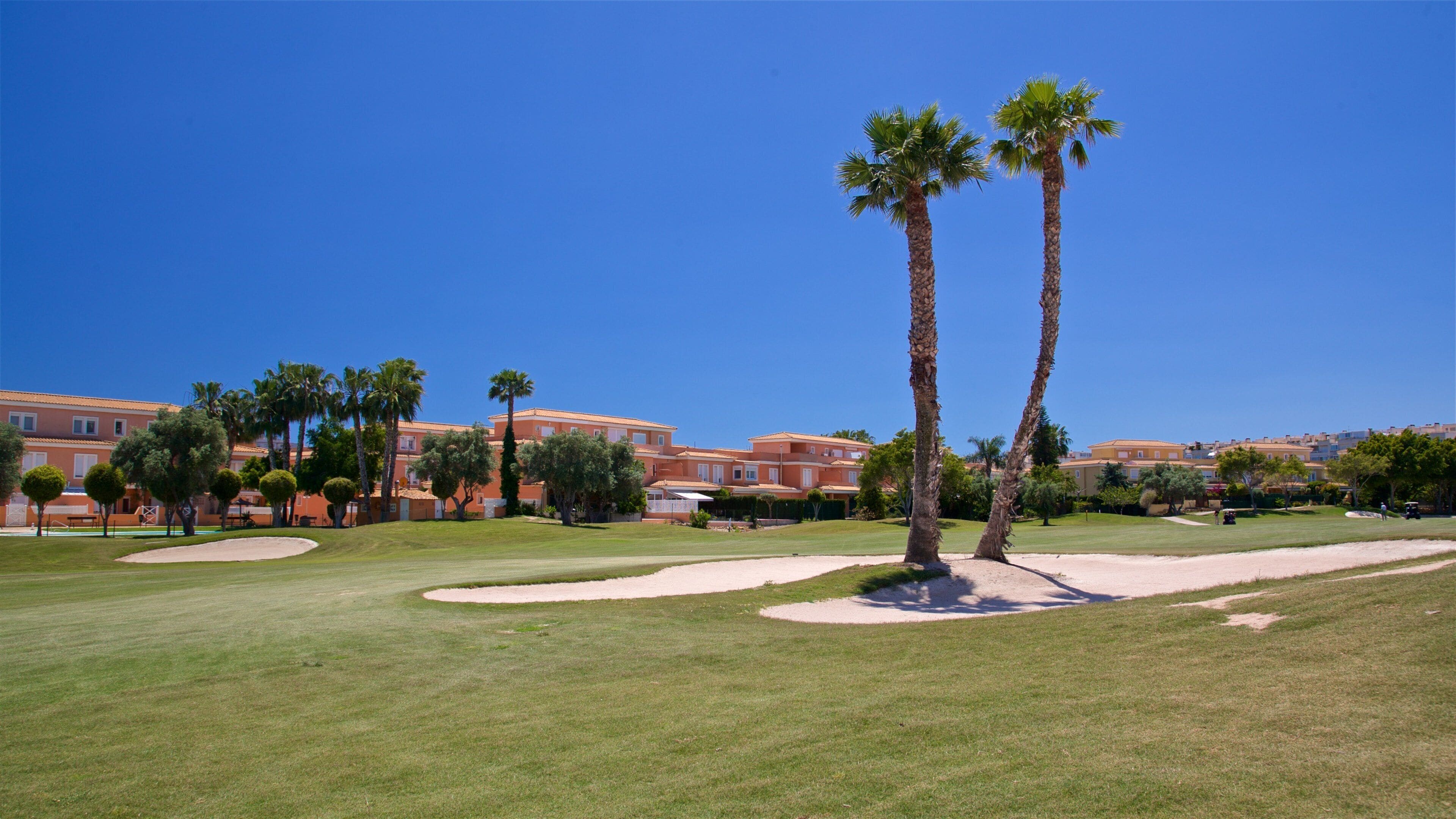 A golf course with sand bunkers, palm trees, and Mediterranean-style buildings.