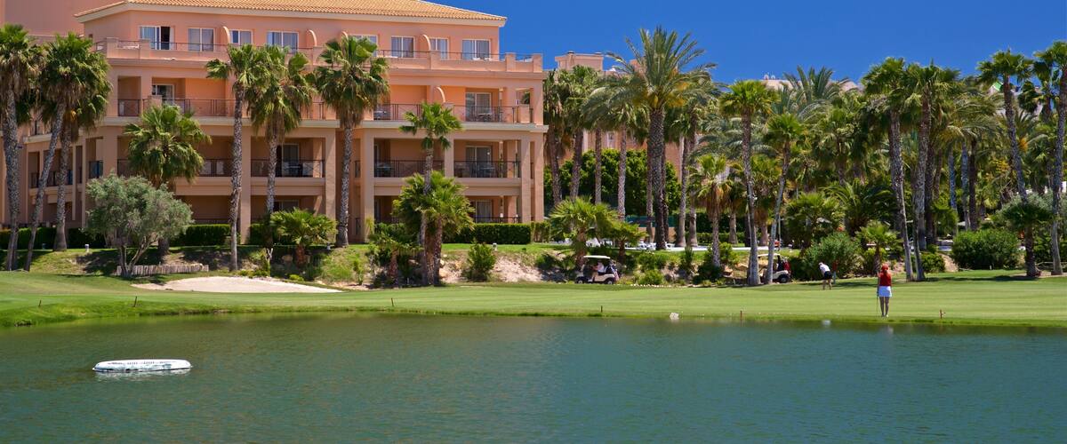 A golf course with a water hazard, palm trees, and a hotel building.