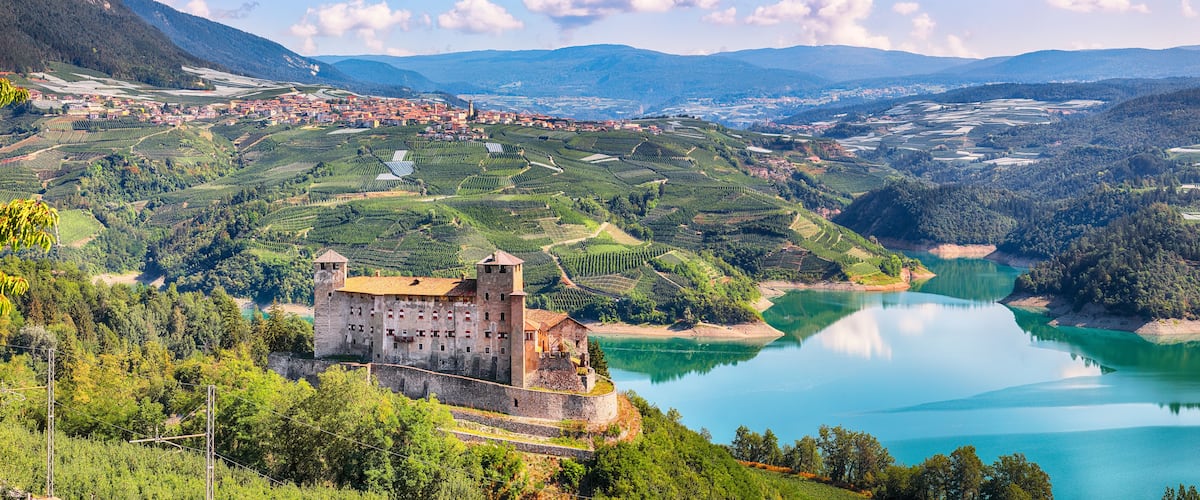 Un château perché sur une colline, dominant un lac, entouré de vignobles et surplombant une ville située dans la vallée.