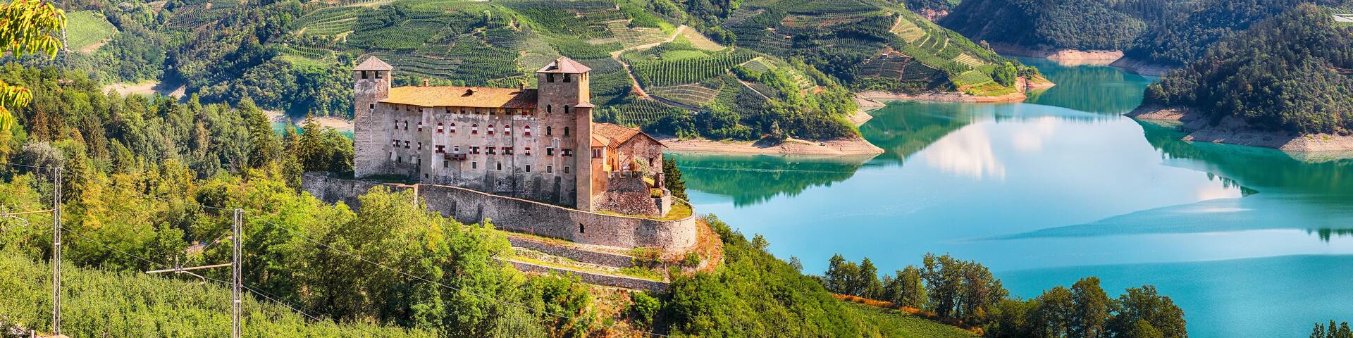 A castle on a hill overlooking a lake, surrounded by vineyards and a town in the valley.