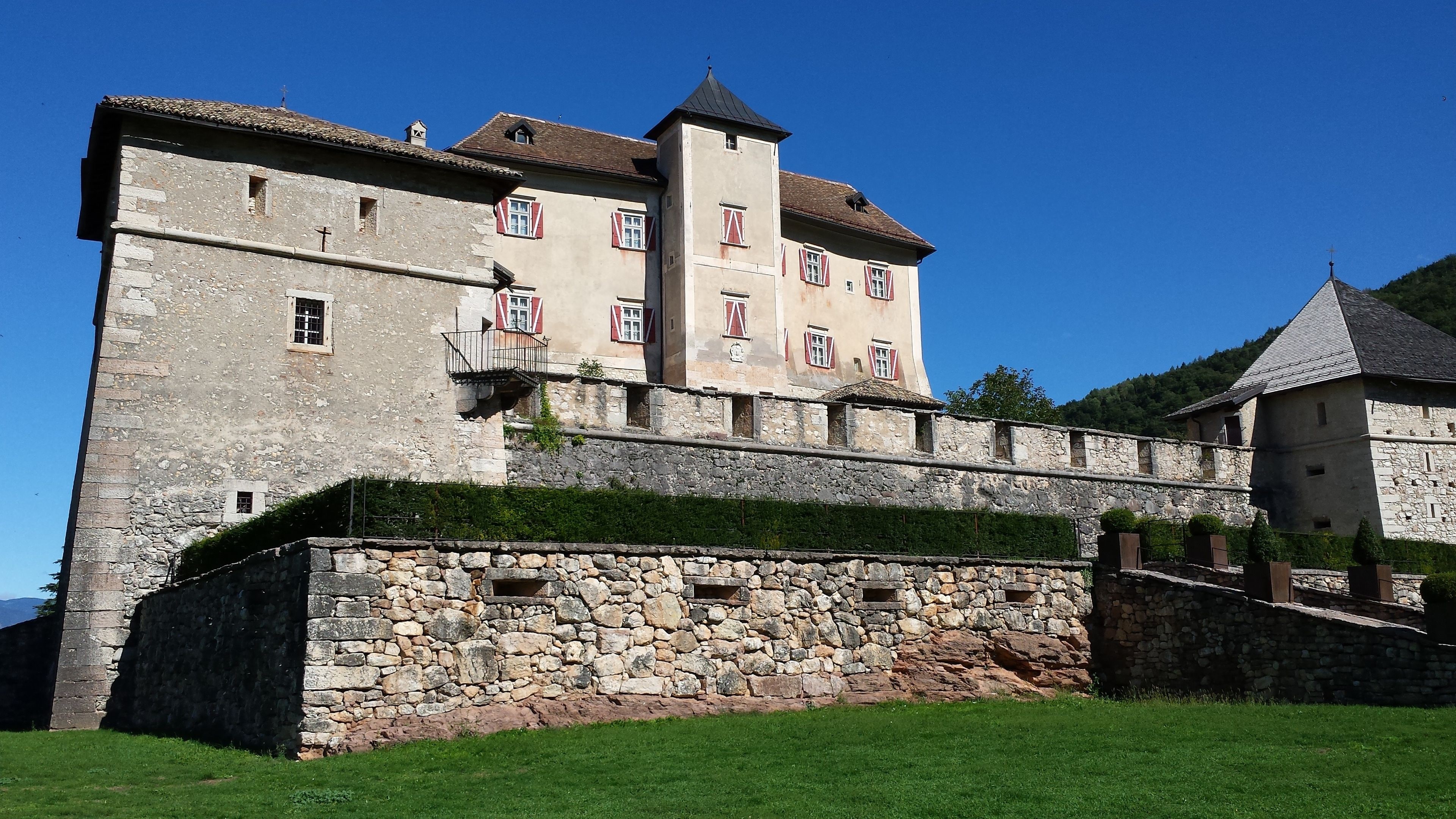 Un castillo histórico con una muralla de piedra y contraventanas rojas.