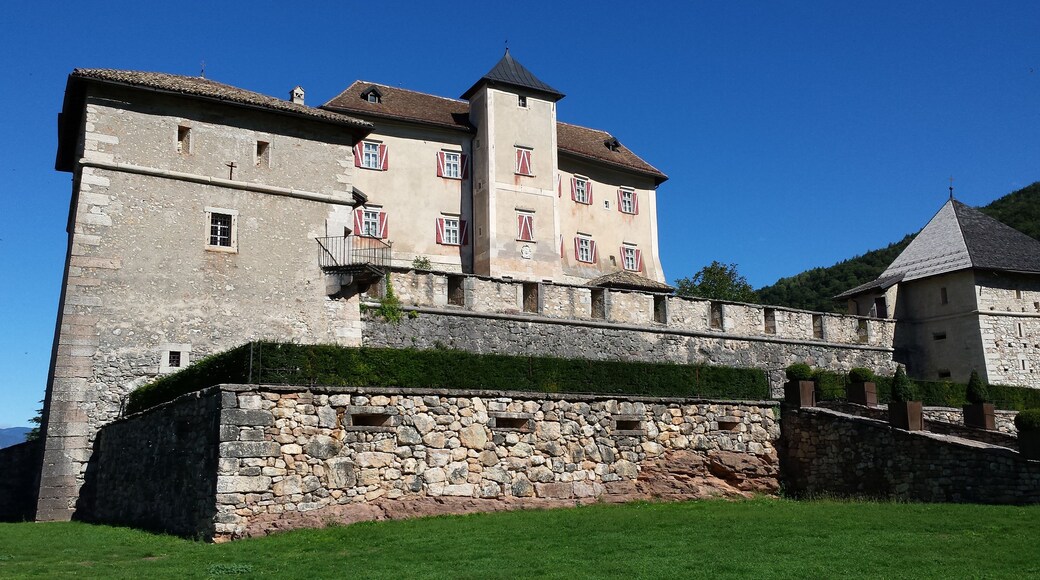 Un castillo histórico con una muralla de piedra y contraventanas rojas.