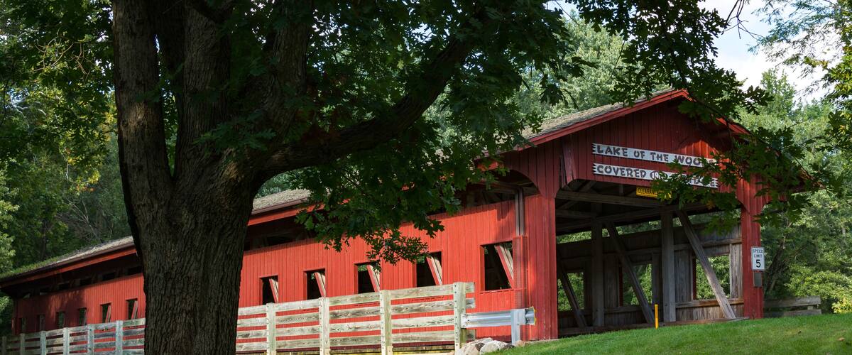 A red covered bridge with a sign that reads "Lake of the Woods Covered Bridge."