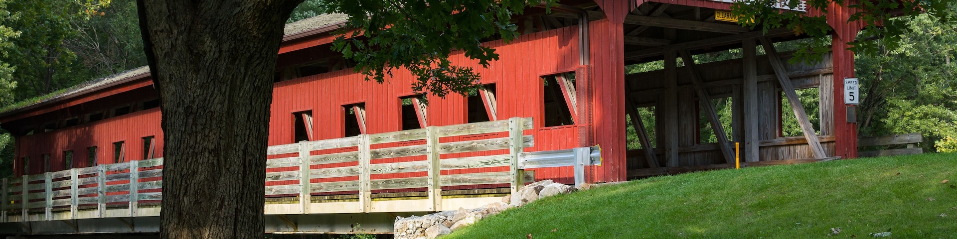 A red covered bridge with a sign that reads "Lake of the Woods Covered Bridge."