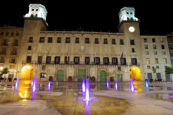 A historic building with two towers and a fountain in the courtyard.