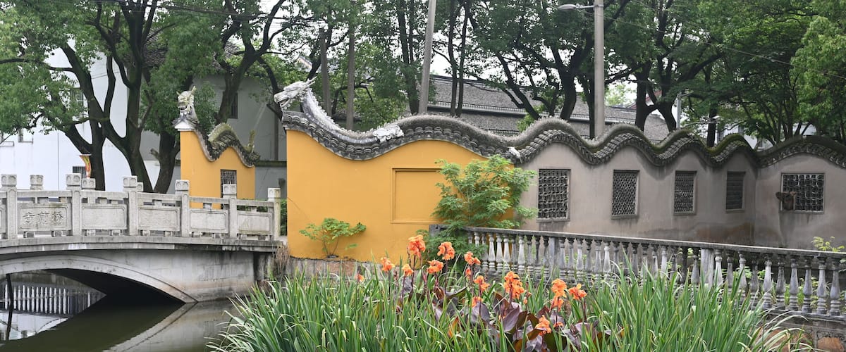 A traditional Chinese bridge over a pond with lotus flowers and a yellow building.