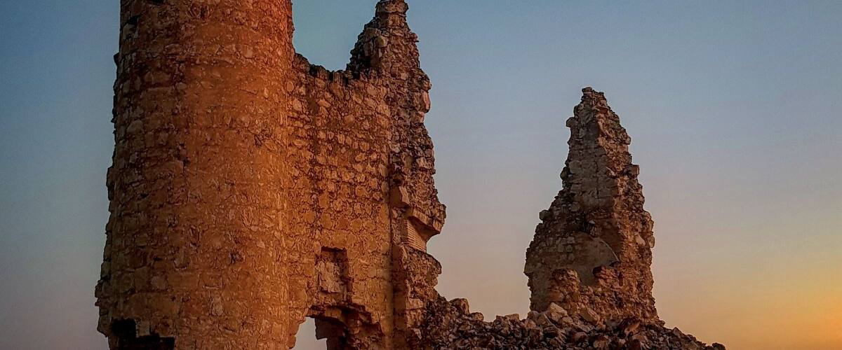 A ruined stone tower with a statue on top, surrounded by rubble and a clear sky.