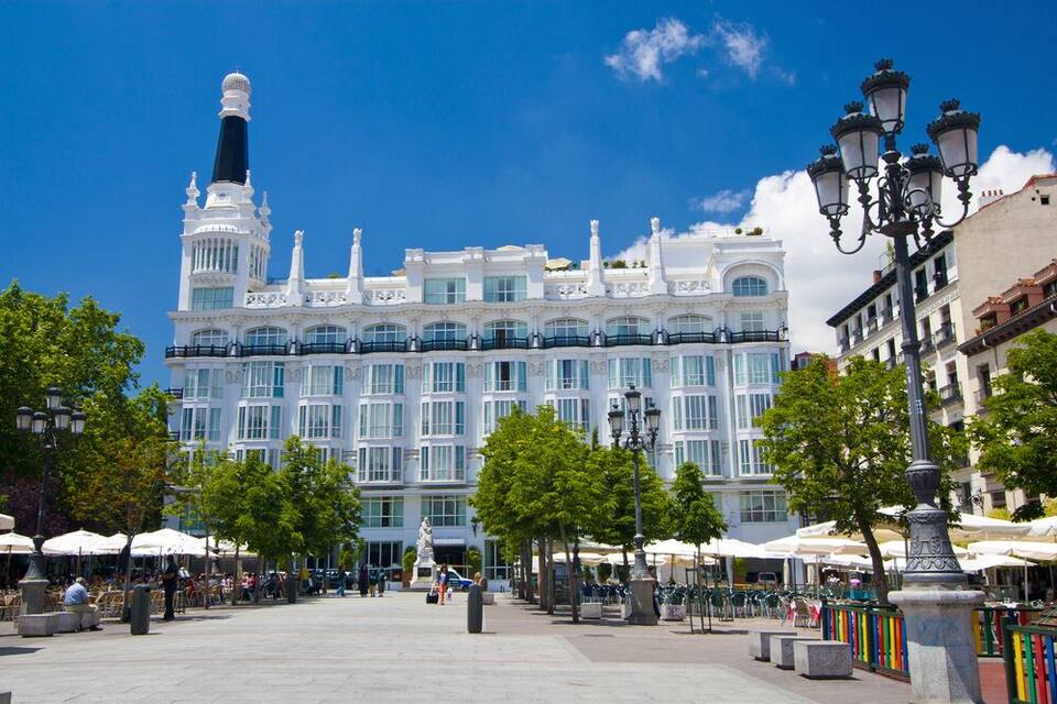Un edificio grande y blanco con una torre, rodeado de árboles y zonas de estar al aire libre.