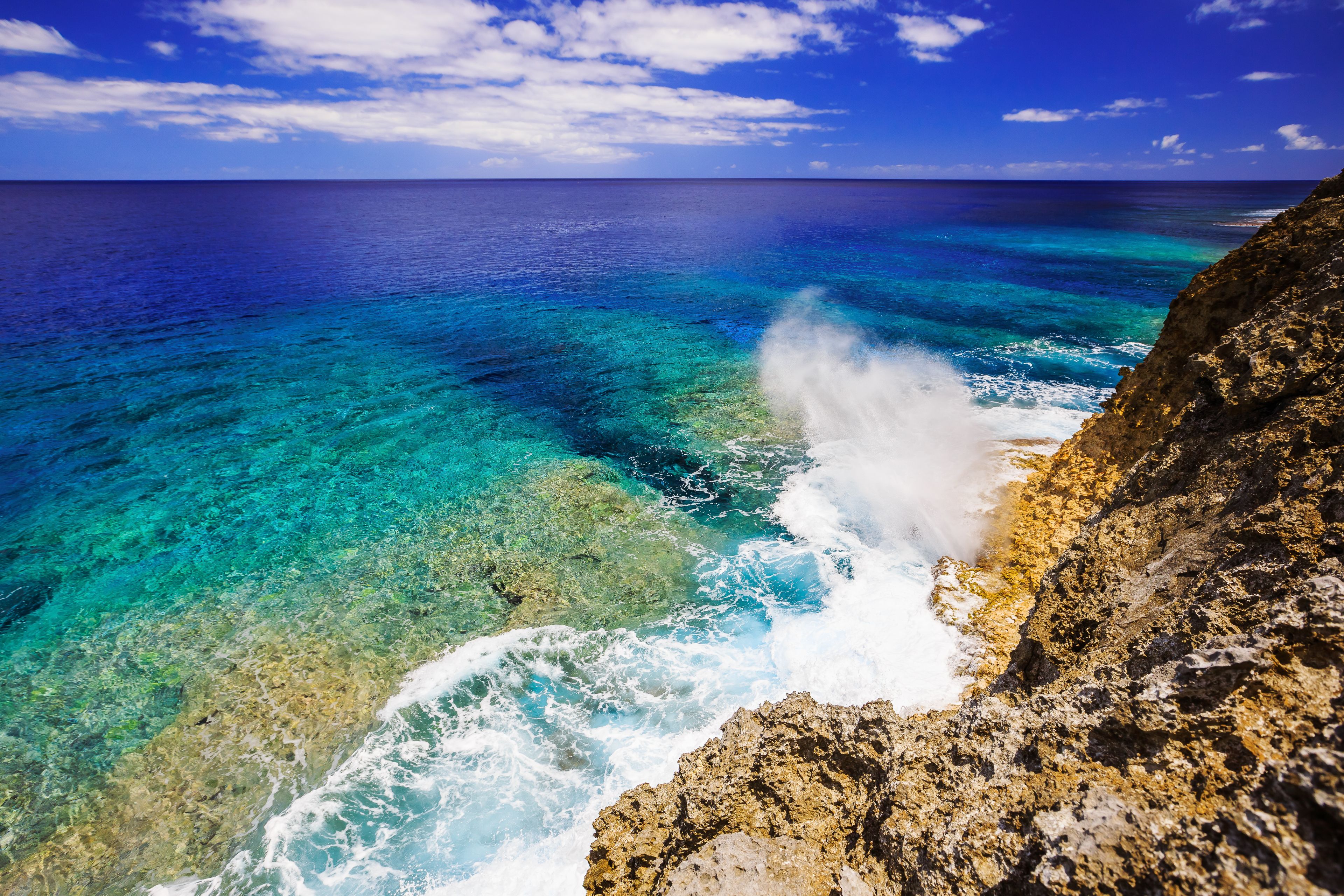 Un paisaje costero con aguas turquesas cristalinas, una costa rocosa y un horizonte lejano bajo un cielo parcialmente nublado.
