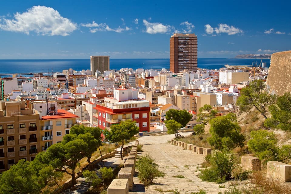 A coastal cityscape with a mix of modern and historic buildings, a clear blue sky, and a view of the sea.