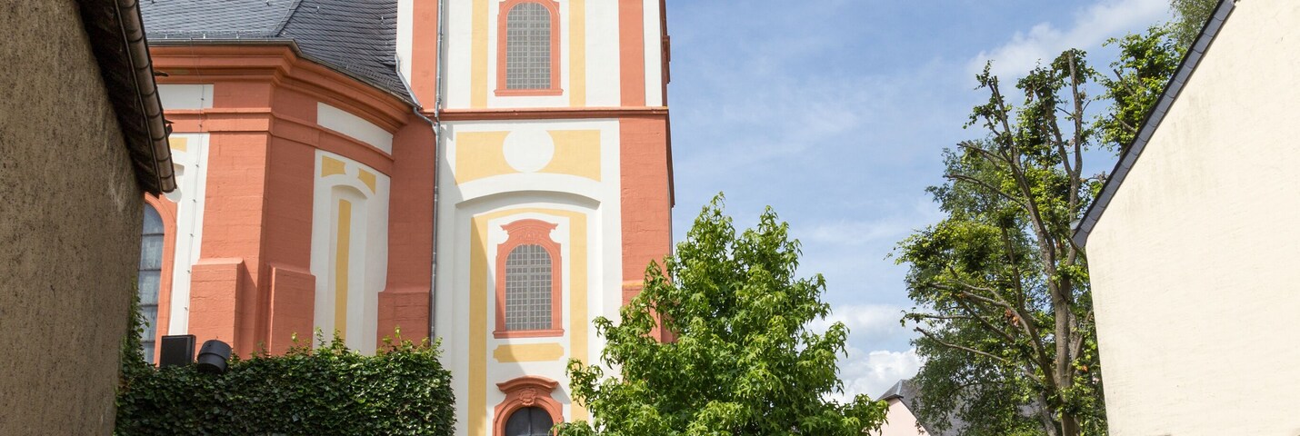 Una iglesia con una torre alta, sendero adoquinado y setos bien cuidados.