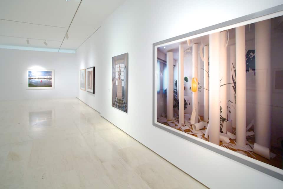 Een kunstgalerie met witte wanden en vloeren, met grote ingelijste kunstwerken en sculpturen.