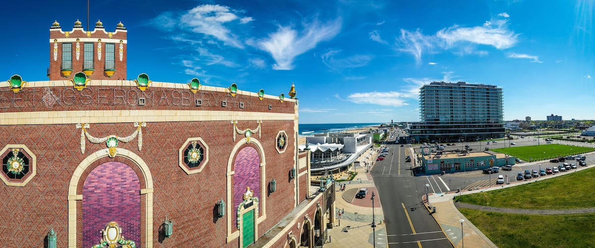 A large brick building with ornate decorations and a clock tower, a modern high-rise building, and a parking lot with cars.