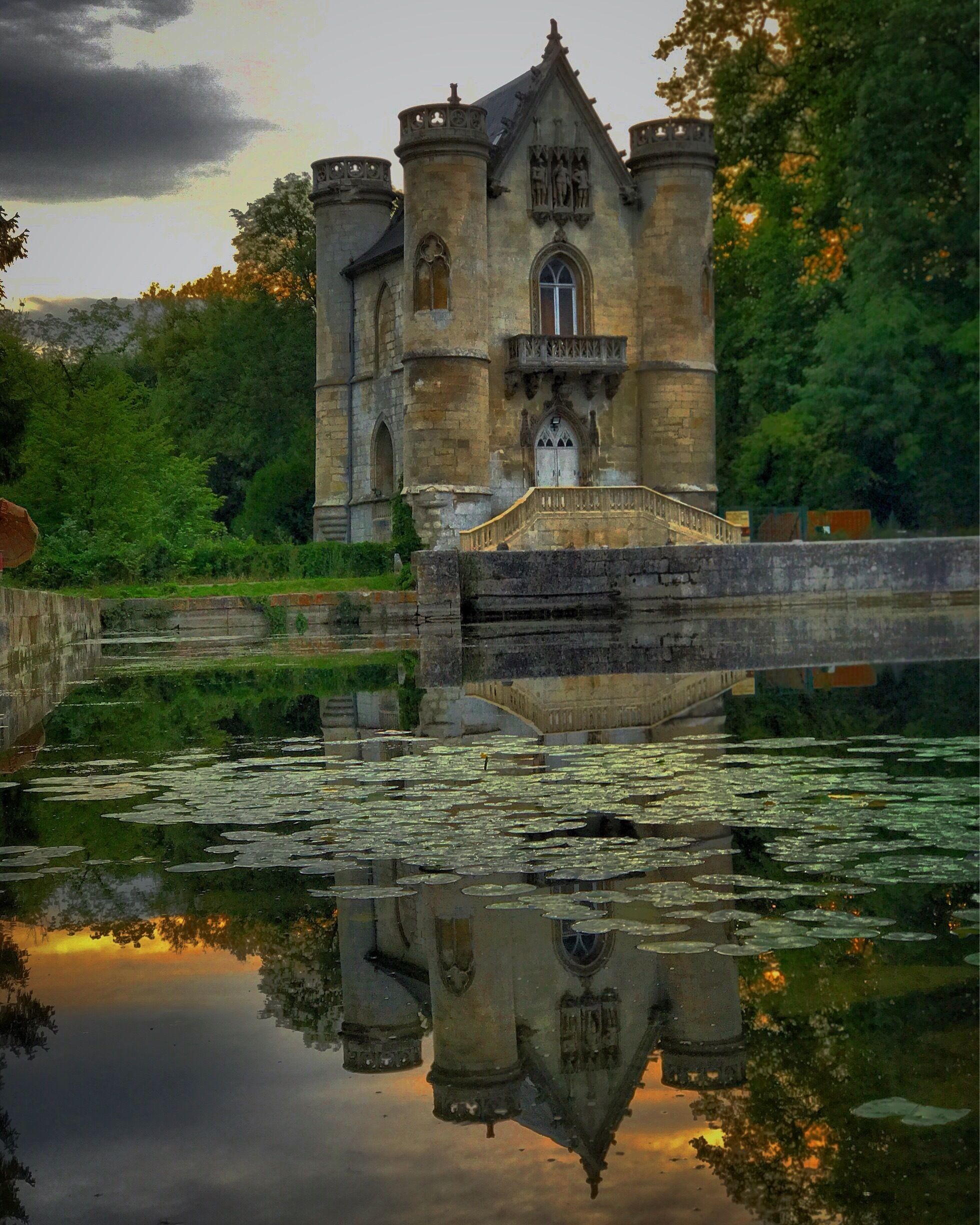 A historic stone castle with a tower, surrounded by lush greenery and a calm river reflecting its structure.