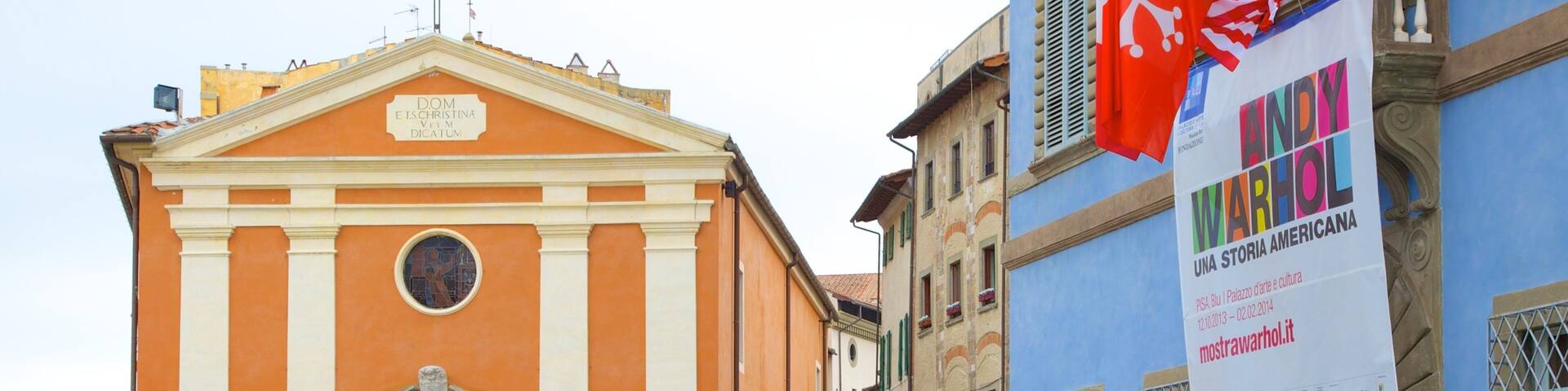 A historic building with a sign reading "DOM ETSCHRISTINA VETM DICATUM" and a colorful banner for "WANDY WARHOL".