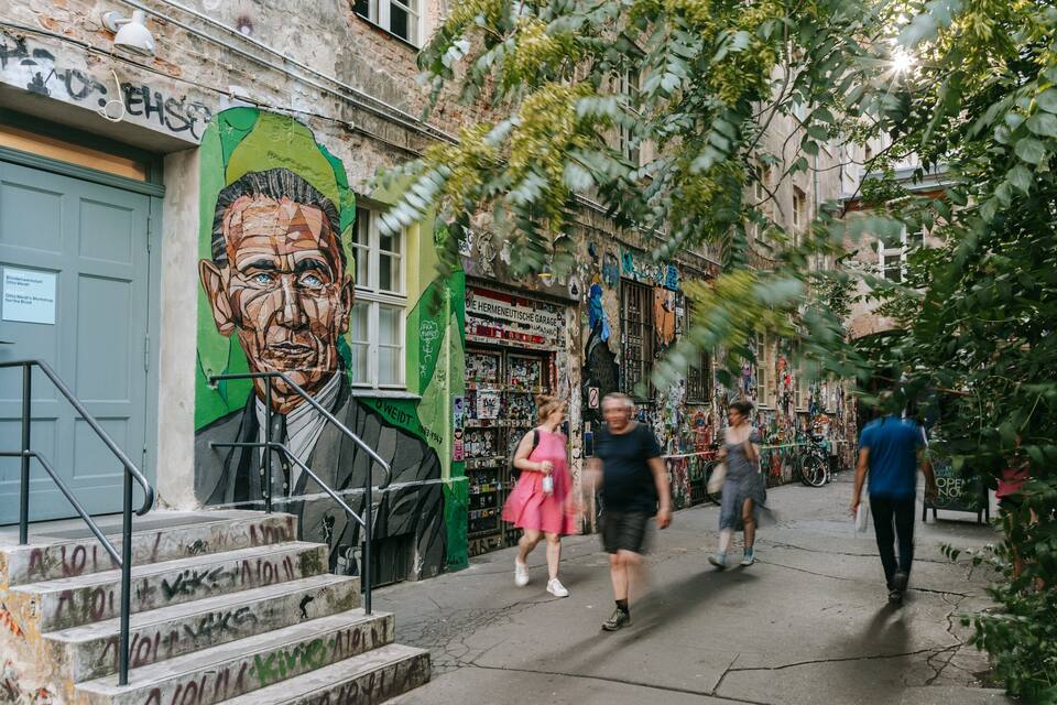 A street with graffiti, a large mural, and a shop with various items.