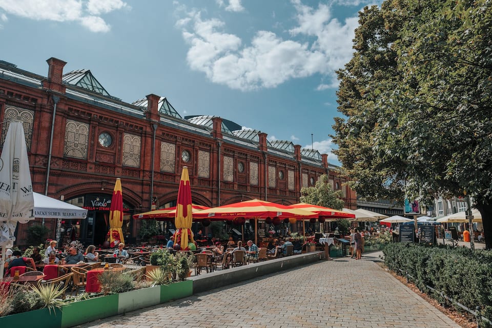 A historic building with ornate architecture and outdoor seating areas with red umbrellas.