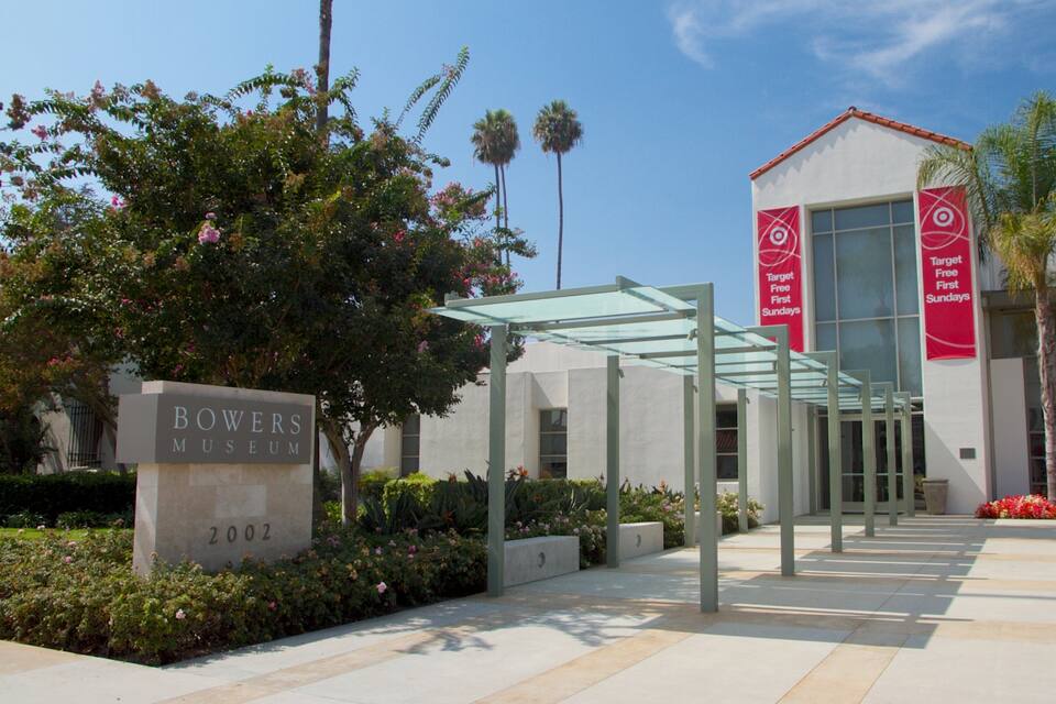 Exterior del Museo Bowes con entrada de vidrio, palmeras y un letrero que indica 'Domingos Gratuitos en Target el Primer Domingo del Mes'.