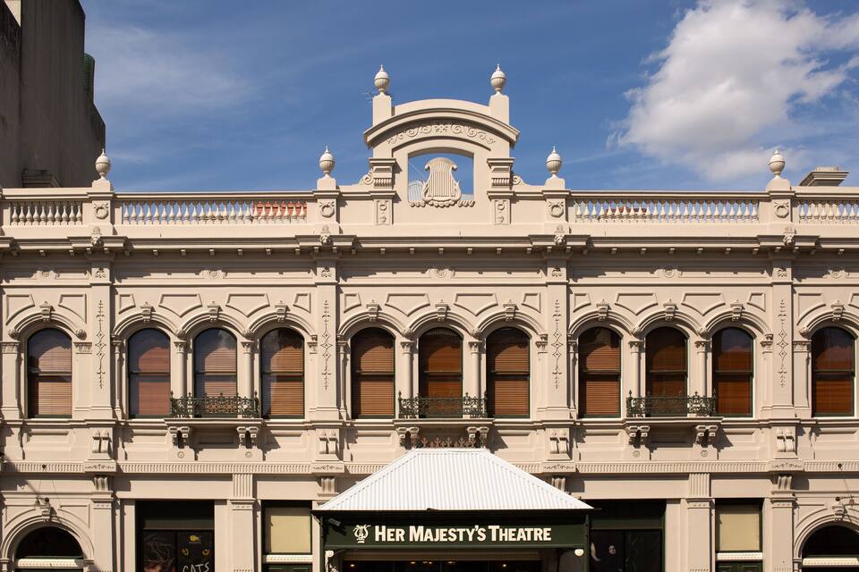 A historic building with ornate architecture, including a balcony and a sign for Her Majesty's Theatre.