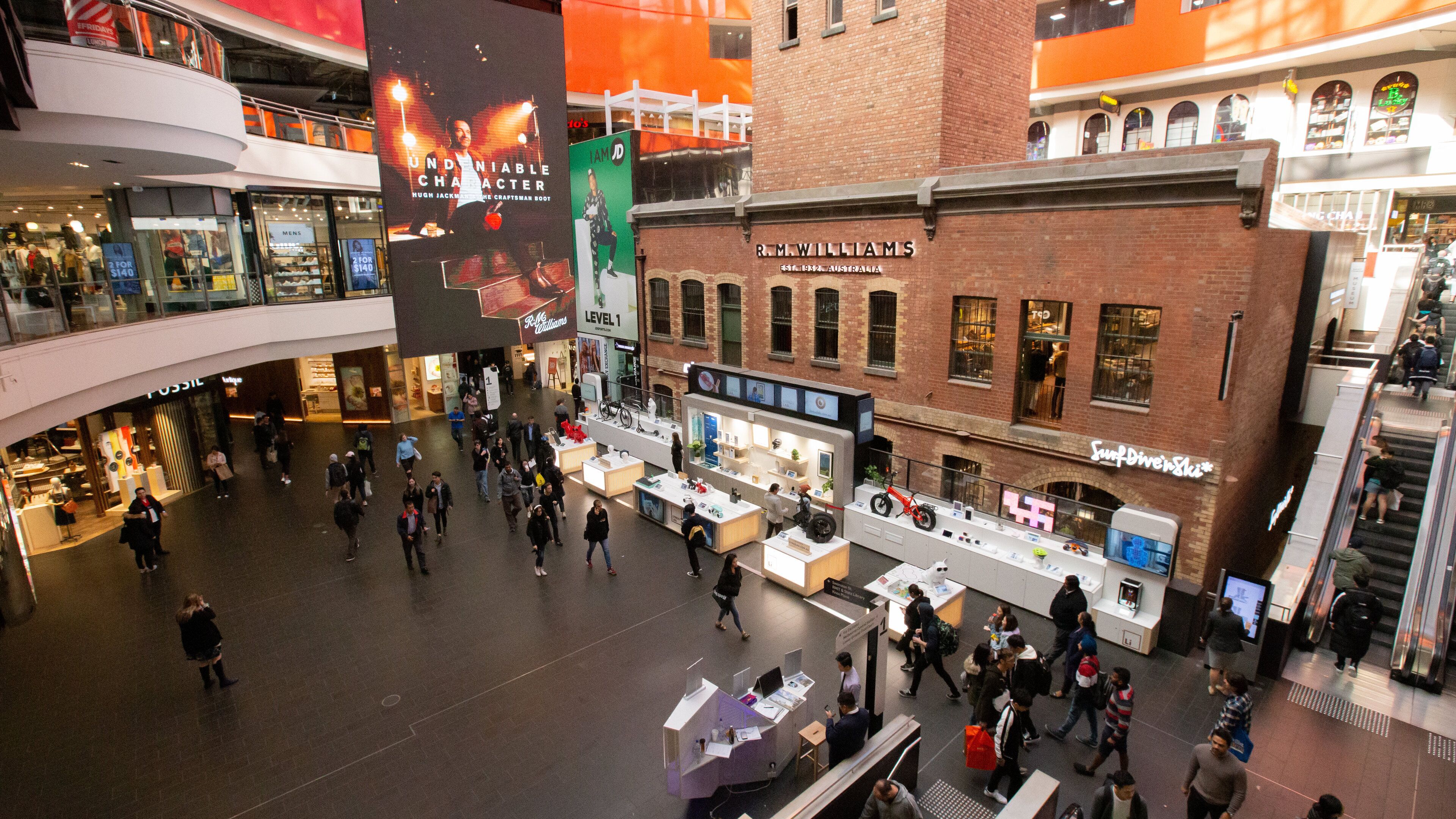 A shopping mall with multiple levels, stores, and a prominent billboard advertising Hugh Jackman.