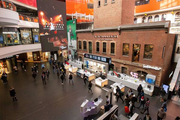 A shopping mall with multiple levels, stores, and a prominent billboard advertising Hugh Jackman.