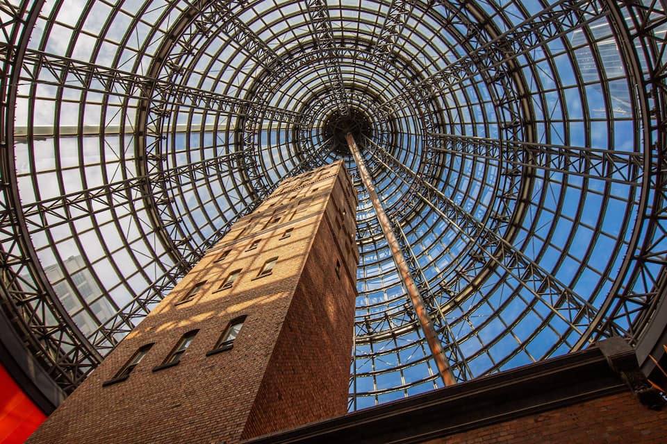 Une vaste structure en forme de dôme de verre, dotée d’une ossature métallique, sous laquelle se trouve un bâtiment en briques.