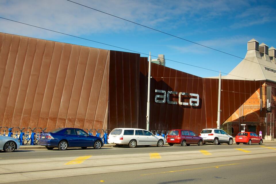 A large brown building with the letters "ACCA" on the side, parked cars, and a clear blue sky.