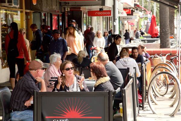 Acland Street which includes outdoor eating and café scenes as well as a large group of people