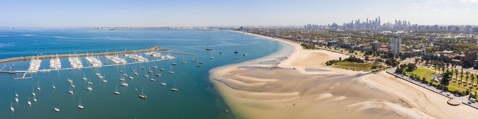 A coastal cityscape with a marina, sandy beach, and urban skyline.